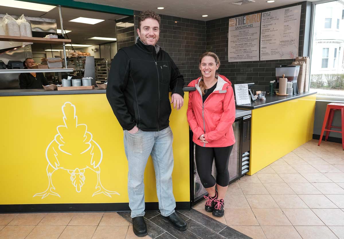This is an image of two people standing in a Flip the Bird restaurant in MA. They are both smiling and ready to experience the best fried chicken and ribs in Swampscott and Beverly MA. Flip the Bird was featured on Wicked Local.