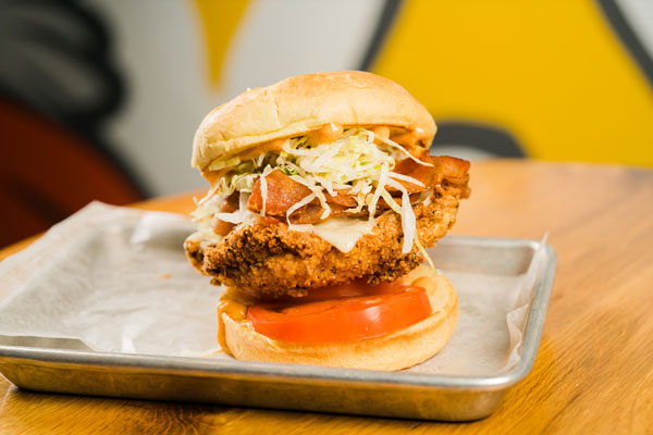 This is an image of a fried chicken sandwich topped with lettuce, cheese, bacon, and tomato. Flip the Bird offers a wide variety of different kinds of fried chicken sandwiches along with having various different locations. These locations include Swampscott and Beverly MA.