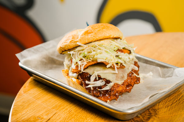 This is an image of a fried chicken sandwich from Flip the Bird. This fried chicken sandwich has various different toppings along with a buttered and grilled potato roll as a bun.